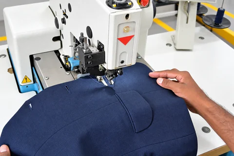 A navy blazer positioned for eyelet buttonhole work at the sewing station.