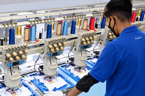 An operator tending embroidered garment panels at a multi-head embroidery workstation.