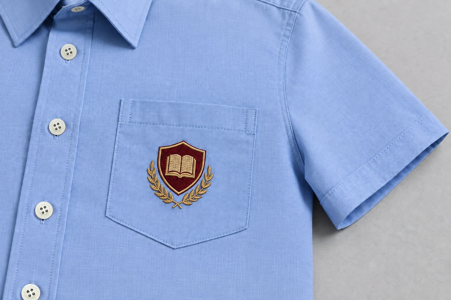 Half-Sleeve School Shirts — powder-blue pocket with burgundy and gold original sample crest. close embroidery detail photograph. Illustrative catalogue concept.