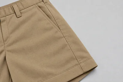 School Shorts — Khaki tailored pocket and hem. macro pocket and hem construction detail photograph. Illustrative catalogue concept.